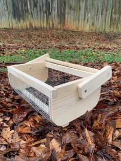 a wooden box with a metal wire in it on the ground surrounded by brown leaves