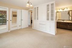 an empty living room with white walls and doors leading to a bathroom area that also has double sinks