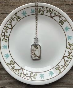 a white plate with a green and blue design on it, holding a small pendant