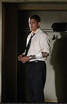 a man in a white shirt and black tie standing next to an open door with his hands on his hips