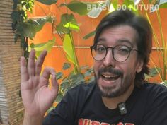 a man with glasses making the vulcan sign in front of an orange wall and green plants