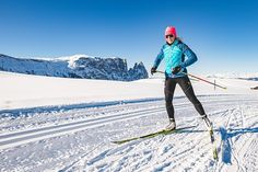 a woman skiing down a snow covered slope with mountains in the backgrouds