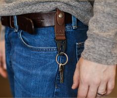 a person wearing a brown leather belt and holding a pair of scissors in their pocket