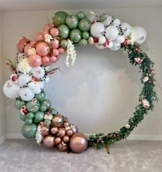 a wreath made out of balloons and greenery is displayed in the corner of a room