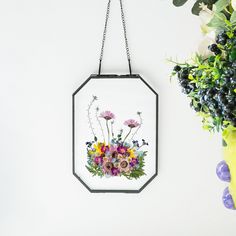 a flower arrangement is hanging from a metal frame on the wall next to a vase with flowers