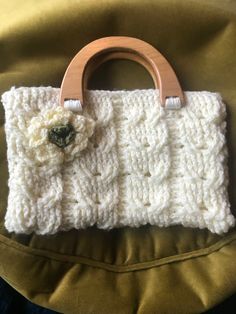 a crocheted purse with a wooden handle and flower on the front, sitting on a green cushion