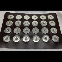 a bunch of buttons sitting on top of a black leather tray with white fabric behind them