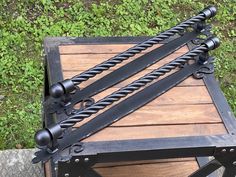 an iron and wood table with two black handles on it's sides, sitting in front of some green grass