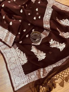 This is a traditional pure banarasi woven georgette saree in beautiful chocolate brown colours with an amazing zari weave. Saree features elegantly floriated zari border and pallu. The floral bootis is run throughout the body of the saree. The pallu has paisley bootis in zari weave, the pallu is finished with skill full tassels, which makes it more beautiful. Georgette gives a very beautiful drape owing to its flowy nature. Color: Chocolate Brown Length: 5.5 Meters Width: 1.2 Meters Blouse: Runn Chocolate Brown Saree, Elegant Georgette Saree With Traditional Patterns, Traditional Handloom Georgette Saree, Traditional Handloom Georgette Dupatta, Elegant Georgette Dupatta With Traditional Patterns, Traditional Georgette Blouse With Zari Weaving, Traditional Wear With Zari Weaving In Georgette, Handloom Georgette Dupatta With Traditional Drape, Semi-stitched Georgette Saree With Traditional Patterns