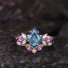 a ring with blue topazte, pink and white sapphires on it sitting on a rock