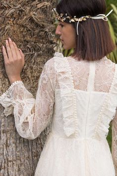 a woman standing next to a tree wearing a white dress and headpiece with flowers in her hair