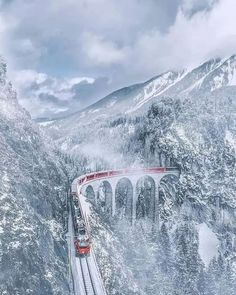 a train traveling over a bridge in the middle of snow covered mountains with trees on both sides