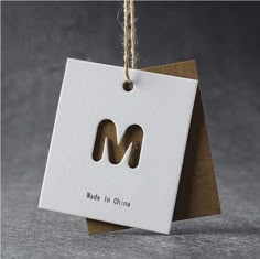 a tag with the letter m hanging from a string on a gray background that says made in korea