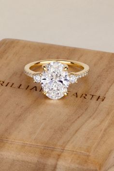 an oval diamond ring sits on top of a wooden box