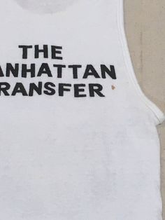 "1970s band tanktop shirt Hanes, cotton, white ribbed The Manhattan Transfer black print Atlantic Records symbol at lower right of image front/back image good vintage condition, light wear light stains, light cracking label size M, see below measures, lying flat, chest-12\" unstretched to 19\" stretched length-26\"" Stretch Cotton Vest With Letter Print, Retro Fitted Crew Neck Tank Top, Fitted Retro Crew Neck Tank Top, Fitted Cotton Muscle Tee With Graphic Print, Retro Fitted Cotton Tank Top, Fitted Retro Cotton Tank Top, Retro White Tank Top For Streetwear, Fitted White Cotton Muscle Tee, Retro Stretch Tank Top With Graphic Print