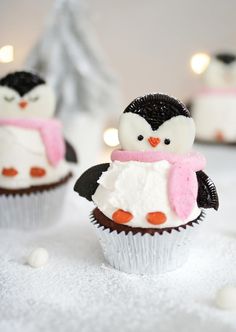 some cupcakes with frosting and penguins on them are sitting in the snow