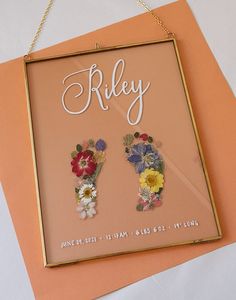 a sign with flowers on it that says riley and is hanging from a gold chain