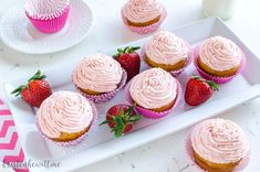 cupcakes with pink frosting and strawberries on a white tray next to a glass of milk