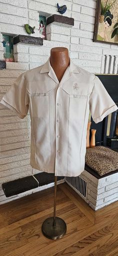 Cool 1970's Polyester ream Short sleeve Shirt! Button front, Two hidden chest pockets and a needlepoint TIKI God above left pocket! 19" across shoulders 10" sleeves 22" across chest 29" shirt Length Great condition " Iolani Hawaii Executive" Label Size Large Retro Camp Shirt With Pockets, Vintage Single Breasted Tops For Spring, Vintage Cream Cotton Shirt, Fitted Beige Shirt With Pockets, Cream Vintage Cotton Shirt, Vintage Single Breasted Button-up Tops, Vintage Shirt With Button Cuffs And Relaxed Fit, Vintage Single-breasted Button-up Tops, Retro Beige Button-up Shirt