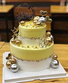 a three tiered cake with gold and silver decorations on the top, sitting on a wooden table