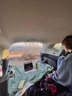 a woman sitting in the back seat of a car looking at a laptop computer on her lap