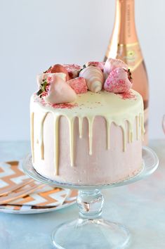 a cake with white icing and strawberries on top next to a bottle of champagne