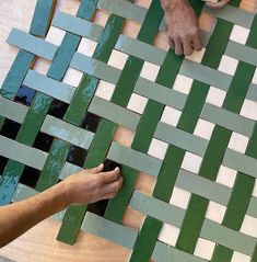 two hands are working on some green and white tiles