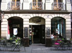 an outdoor cafe with tables and chairs in front of the entrance to a building on a city street