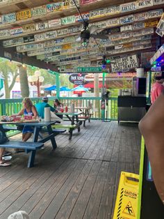 several people sitting at picnic tables under a covered area with many signs on the ceiling