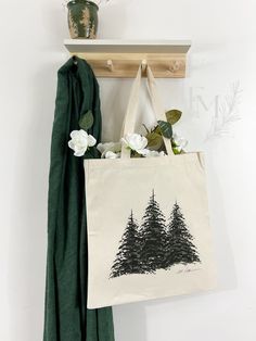 a tote bag hanging on the wall next to a coat rack with flowers in it