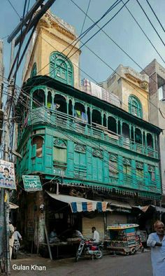 an old building is painted green and has people on the street in front of it