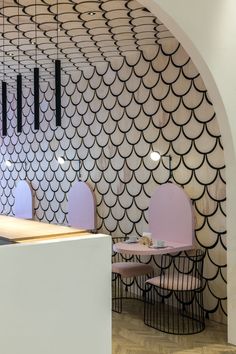 the interior of a restaurant with black and white fish scales on the wall, along with pink chairs