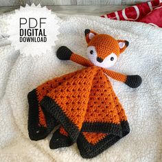 an orange and black knitted animal laying on top of a white blanket next to a red pillow