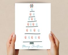 two hands holding up a card with a christmas tree on it and the words merry christmas