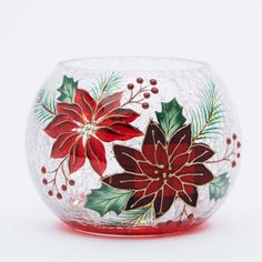 a glass vase with red flowers and green leaves on the inside, sitting on a white surface