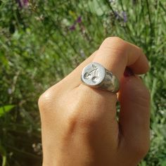 a person holding a ring with the letter c on it in front of some flowers