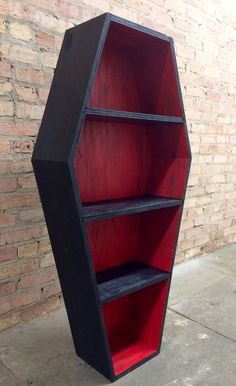 a black and red book shelf sitting on top of a cement floor next to a brick wall