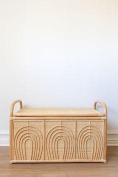 a wooden bench with wicker design on the top and bottom, in front of a white wall