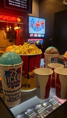 two buckets of ice cream and three cups of popcorn sit on a table in front of a neon sign