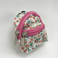 a small white and pink flowered purse with two zippers on each side, sitting on a white surface