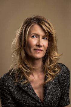 a woman with blonde hair and blue eyes posing for a headshot in front of a brown background