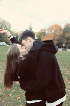 a young man and woman kissing in the park with autumn leaves on the ground behind them