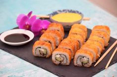 sushi rolls and dipping sauce on a black slate board with purple orchids in the background