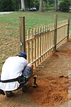 a man kneeling down next to a wooden fence