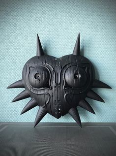 a black mask with spikes and eyes on a blue wall in front of a green background