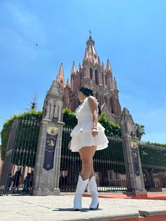 a woman in white dress and cowboy boots standing on the sidewalk next to a tall building