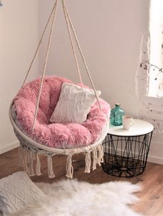 a pink hanging chair in a room with white rugs and pillows on the floor