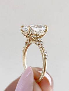 a person holding a gold ring with an oval cut diamond on it's side