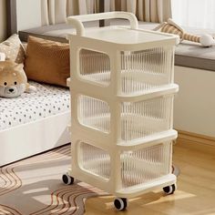 a white plastic storage cart sitting on top of a wooden floor next to a bed