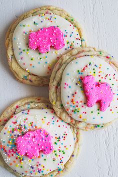 three decorated cookies with pink frosting and sprinkles on a white surface